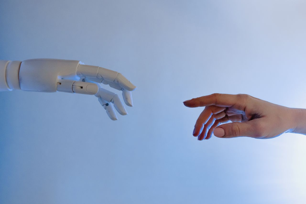 Home A human hand reaching towards a robotic hand symbolizing technology and connection.